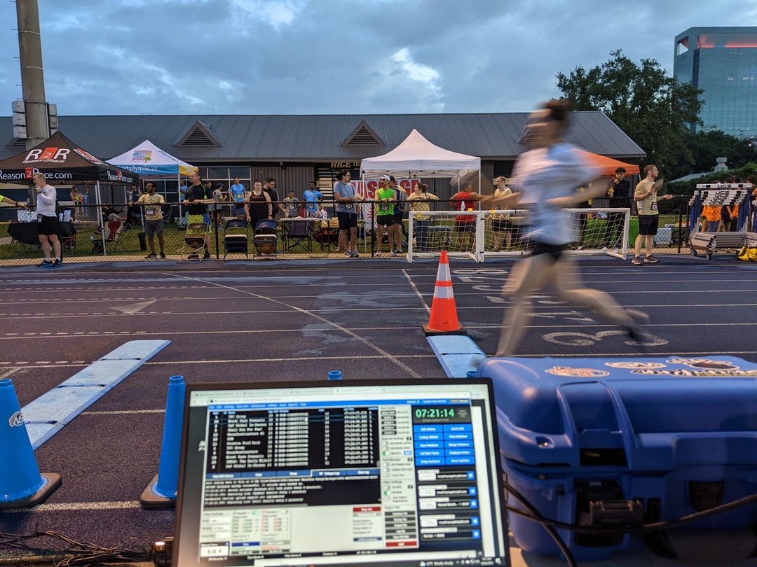 Timing laptop and race clock at the finish as a runner passes on the track