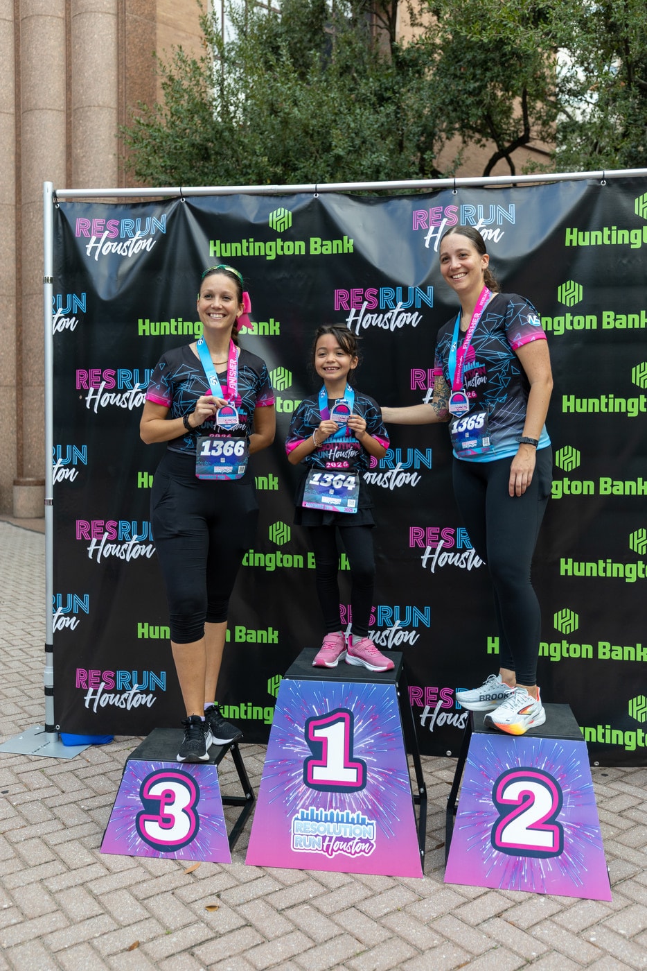 Three finishers on a branded awards podium in front of a sponsor backdrop