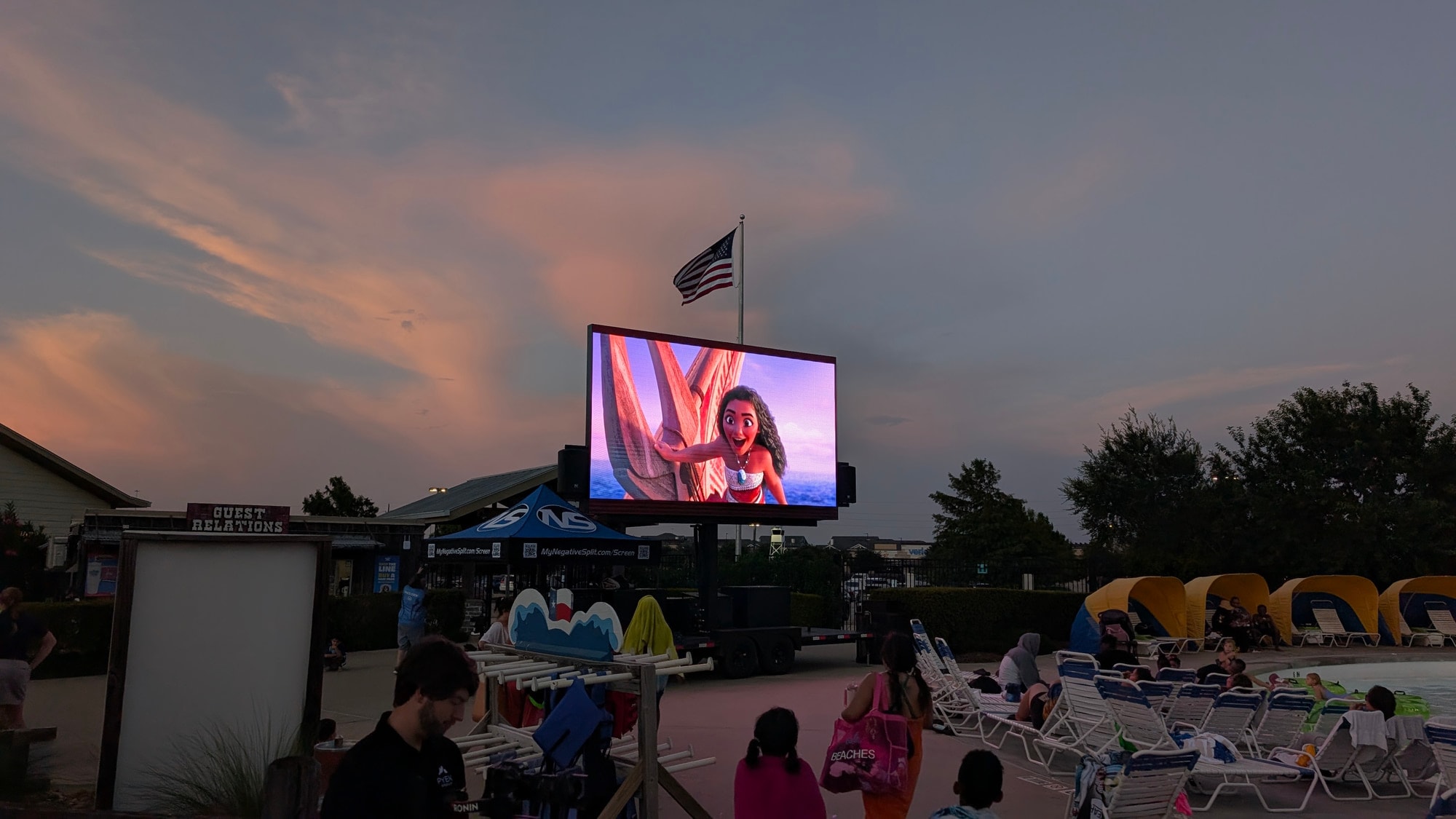 The screen playing a film at dusk over a pool deck of lounge chairs